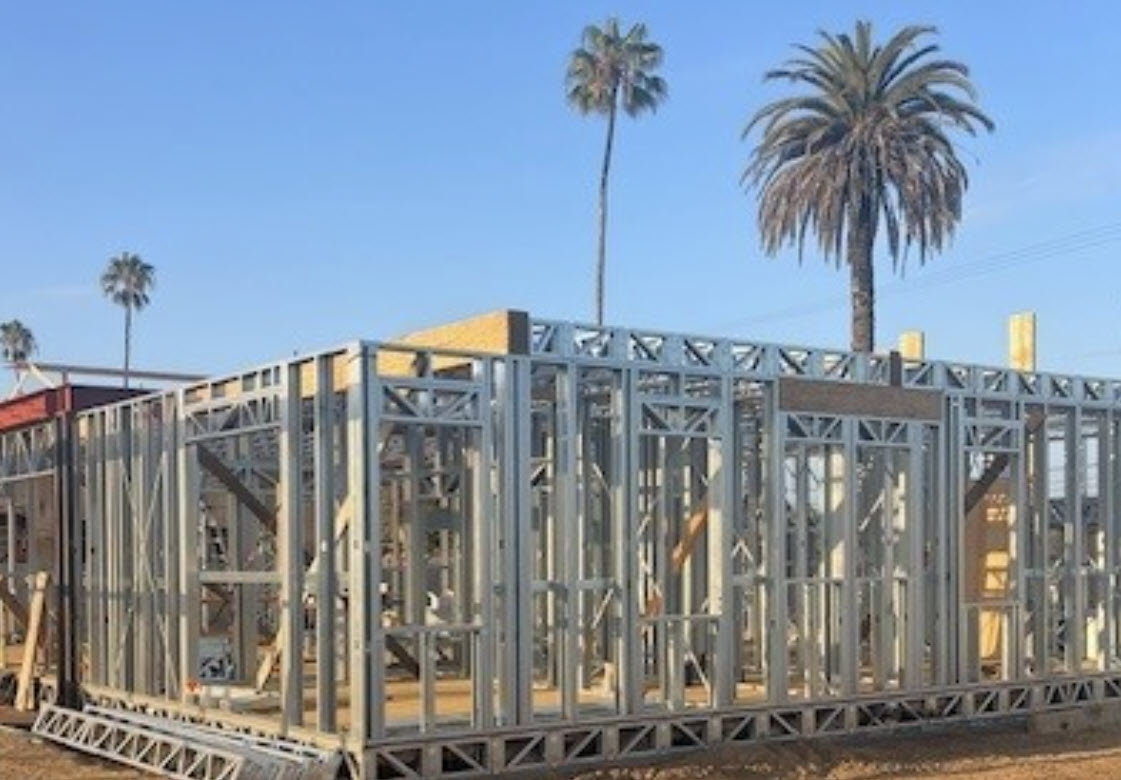 Cold-formed steel wall framing under construction beside palm trees.