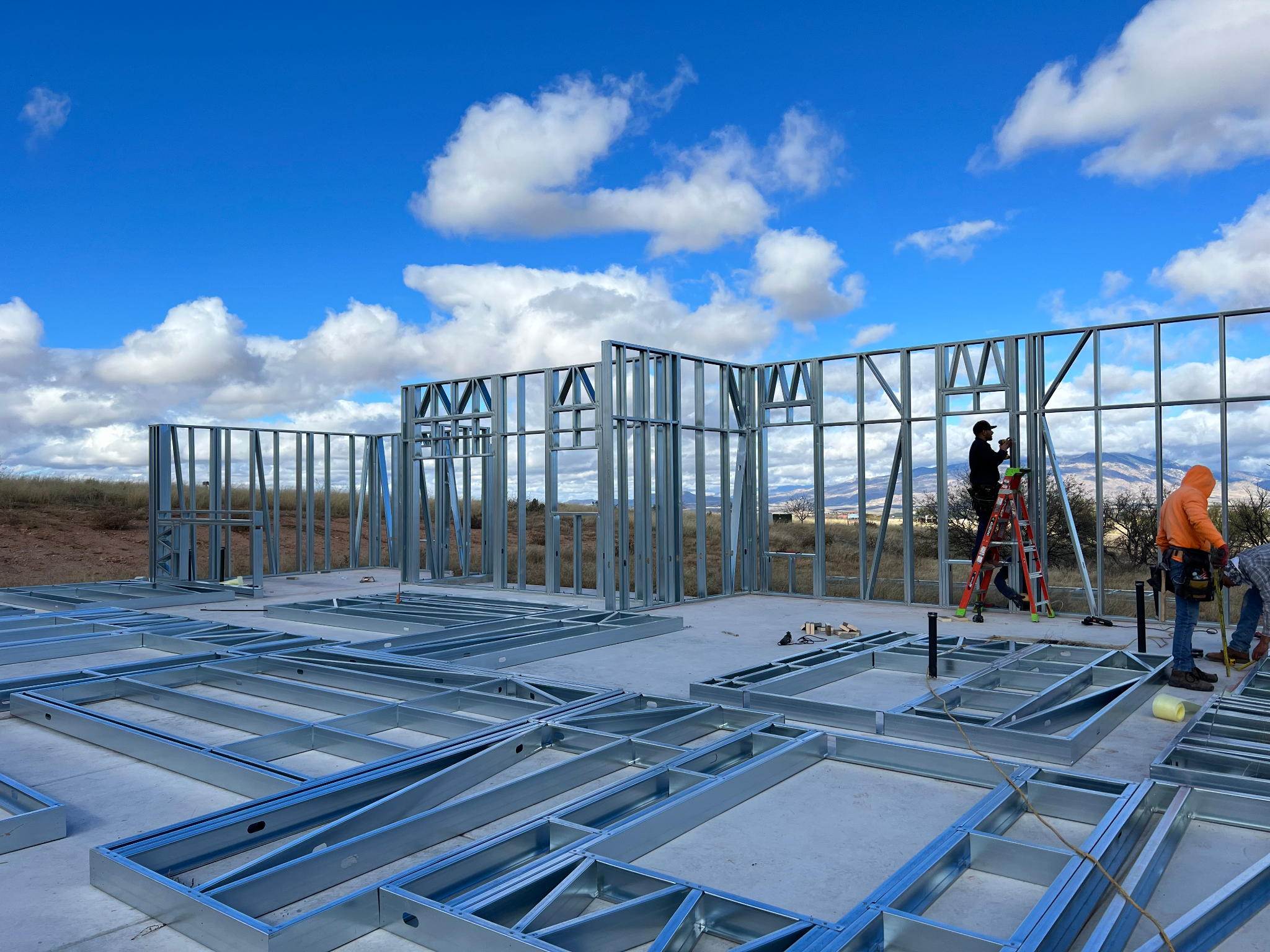 Steel wall panels laid out for assembly beside erected framing.
